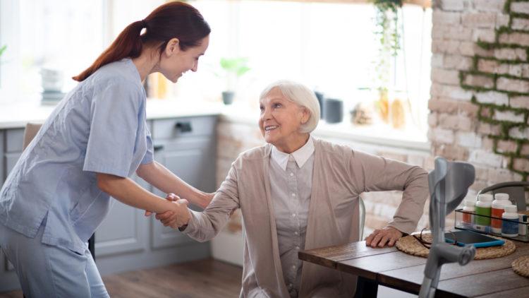 Pleasant caregiver helping aged woman to stand up